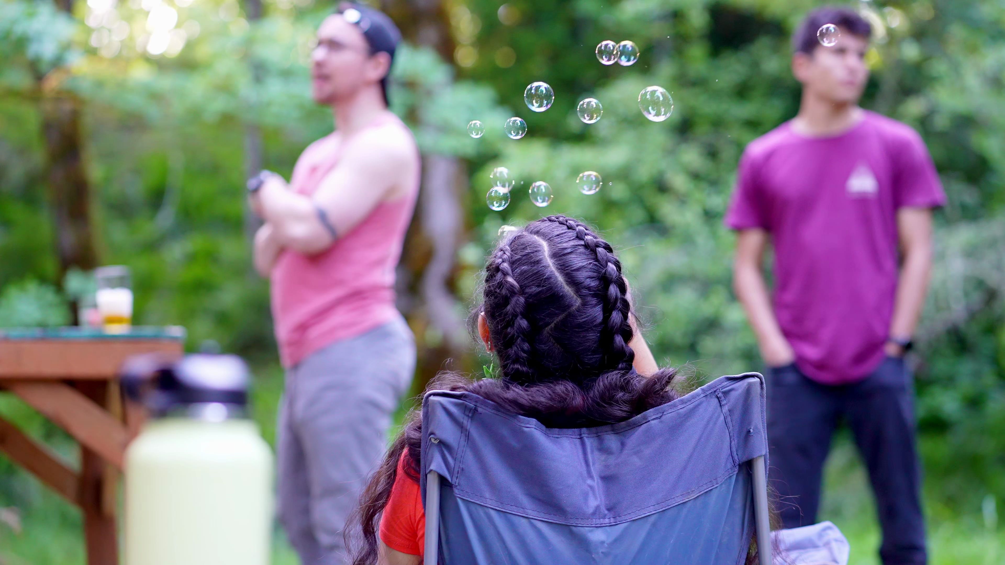Woman with French braids blowing bubbles in a sunlit forest clearing