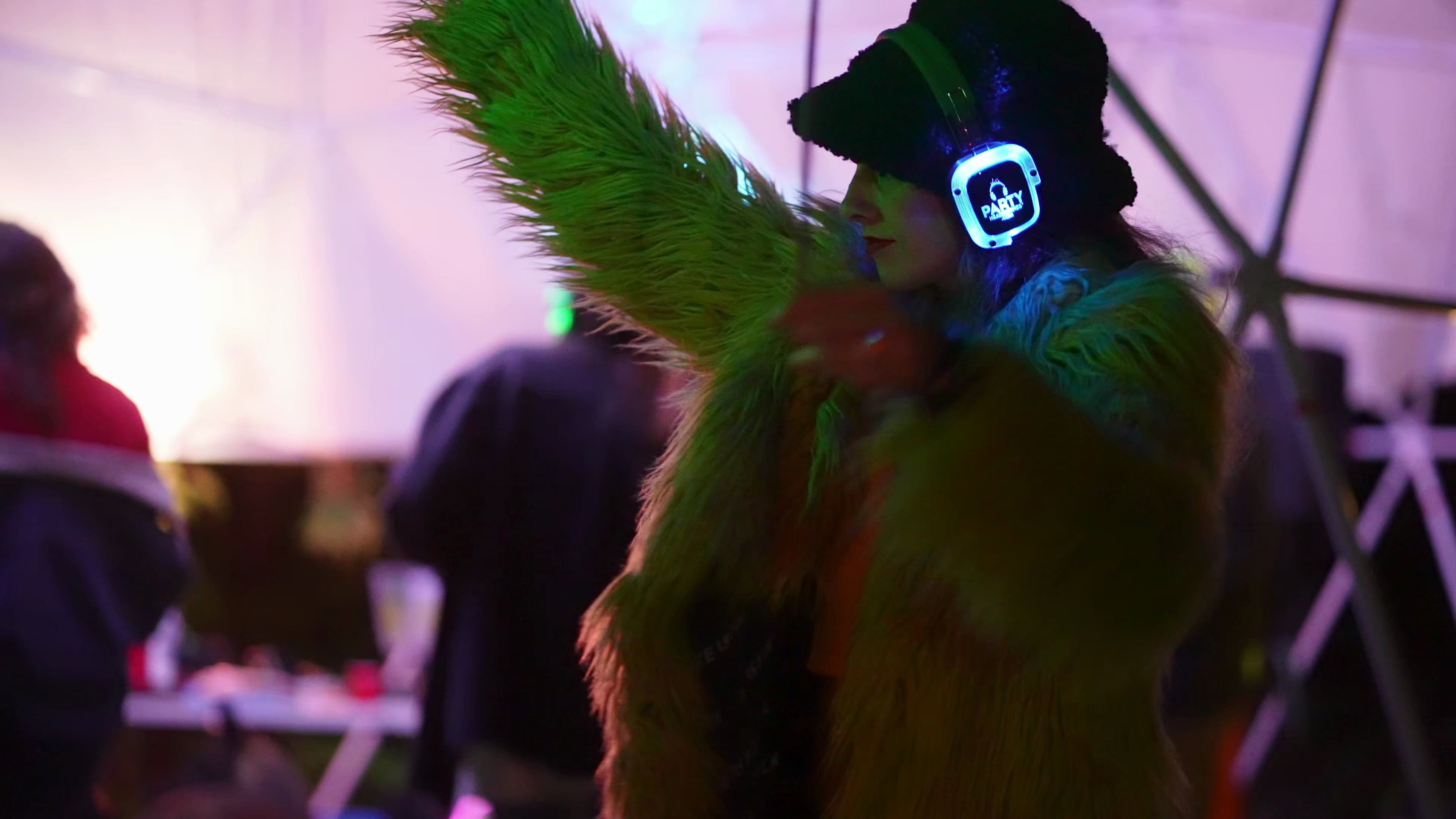 Festival attendee in green feathered outfit with glowing headphones inside a geodesic dome